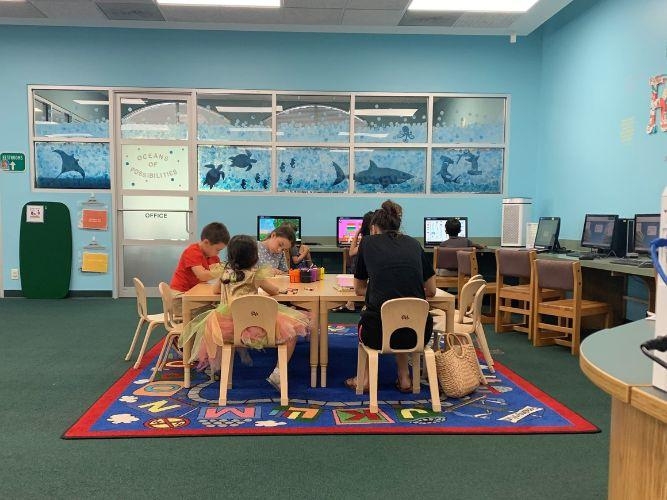 A group of kids studying inside a library with one adult present.
