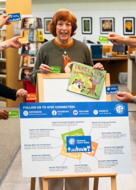 Library Director Debra Rhodes Gibson holding a book crazy like a fox next to a library card infographic. A variety of hands are holding library cards around her.