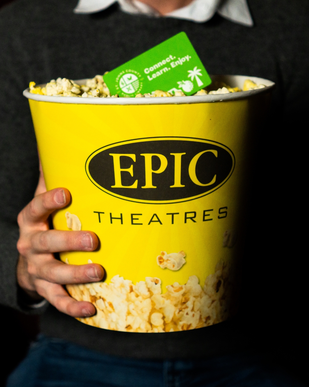 A person holds a large yellow bucket of popcorn labeled 