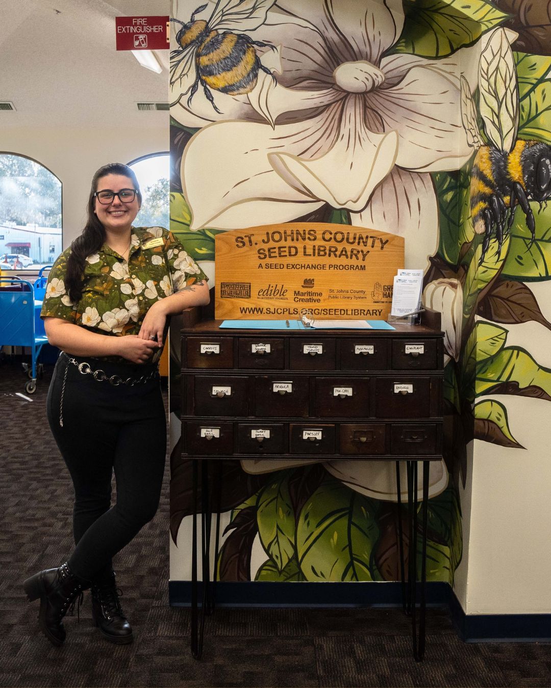 A smiling person in a floral shirt stands beside a vintage drawer labeled 